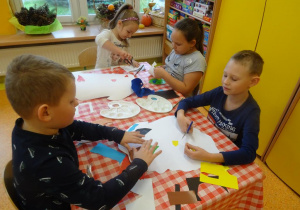 Czwórka dzieci wykleja kontur Polski wyciętymi elementami z papieru.